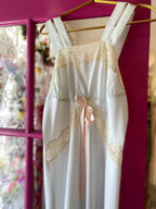 Pale blue vintage slip dress with tan lace trim and pink bow detail hanging on gold hanger