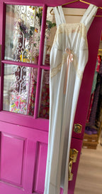 Pale blue slip dress with cream lace and pink bow detail hanging on a pink door in a boutique setting