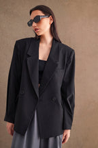 Woman wearing oversized black blazer and sunglasses styled with a black top and gray skirt in minimalist setting