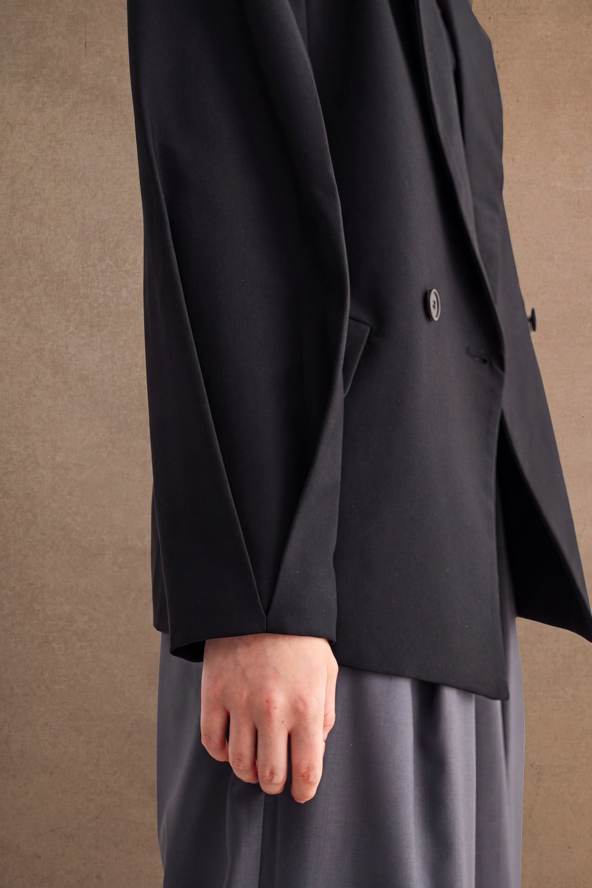 Woman wearing an oversized black blazer paired with loose gray pants in a minimalist setting.