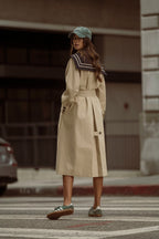 Woman wearing a beige trench coat with a dark collar detail and green cap walking on a city street