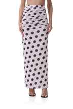 Women's long pink skirt with large black polka dots and ruched detailing at the waist, styled with heels.