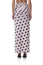 Back view of a woman wearing a long pink skirt with black polka dots and ruched detailing at the waist