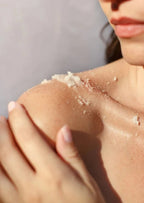 Close-up of woman applying natural body scrub on her shoulder and upper chest skin.