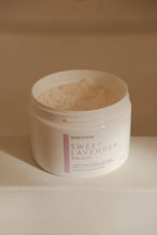 Open jar of natural body scrub with sweet lavender scent on neutral background