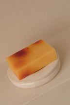 Handmade warm-toned soap bar with subtle natural hues resting on a smooth white ceramic dish