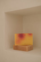 Two handmade bars of natural soap stacked on a beige shelf with a warm, minimal background.
