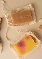 Two handmade soap bars with HEARTSPRING embossed, placed on drawstring pouches on a neutral background