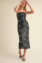 Woman wearing a black strapless midi dress embellished with sequined bow patterns and black high heel sandals.