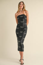Woman wearing a black strapless midi dress with bow-shaped sequin details and black high-heeled sandals