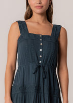 Woman wearing a dark blue tiered midi dress with embroidered lace trim and button front tie waist detail
