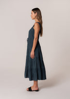 Woman wearing a sleeveless tiered midi dress with lace trim and a tie waist in dark blue for women's clothing.