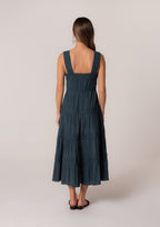 Woman wearing dark embroidered lace trim tiered midi dress with wide straps shown from the back in women's clothing style.