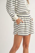Woman wearing cream and black striped cotton shorts and matching long sleeve top with hands in pockets