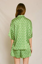 Woman wearing green silky shorts and shirt set with white fish print, shown from the back in women's clothing style.