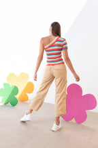 Woman wearing beige wide-leg pants and colorful striped one-shoulder top in a bright studio setting