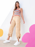 Woman wearing beige cargo pants and a colorful striped one-shoulder top in a minimalist setting