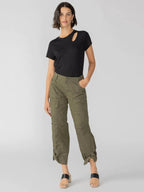 Woman wearing olive green cargo pants with pockets and a black short-sleeve top, standing against a gray background.