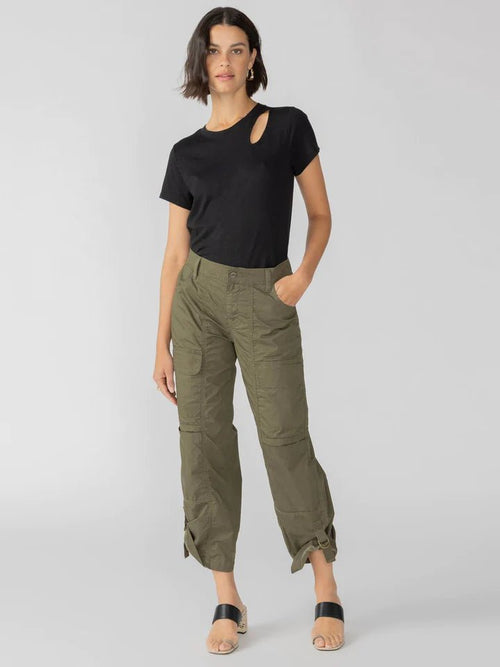 Woman wearing olive green cargo pants with pockets and a black short-sleeve top, standing against a gray background.