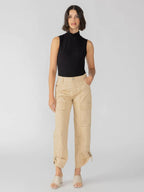 Woman wearing beige cargo pants with ankle ties and a sleeveless black top posing against a plain background