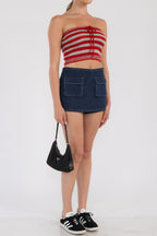 Woman wearing a red and gray striped crop tube top paired with a dark denim mini skirt and black sneakers.