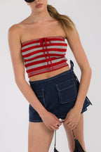 Woman wearing a red and gray striped crop tube top paired with dark blue denim shorts with pockets.