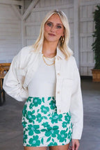 Woman wearing an oversized cream denim jacket over a white top and green floral skirt in a casual setting