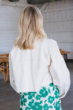 Woman wearing an oversized cropped white denim jacket over a green floral skirt in an indoor setting