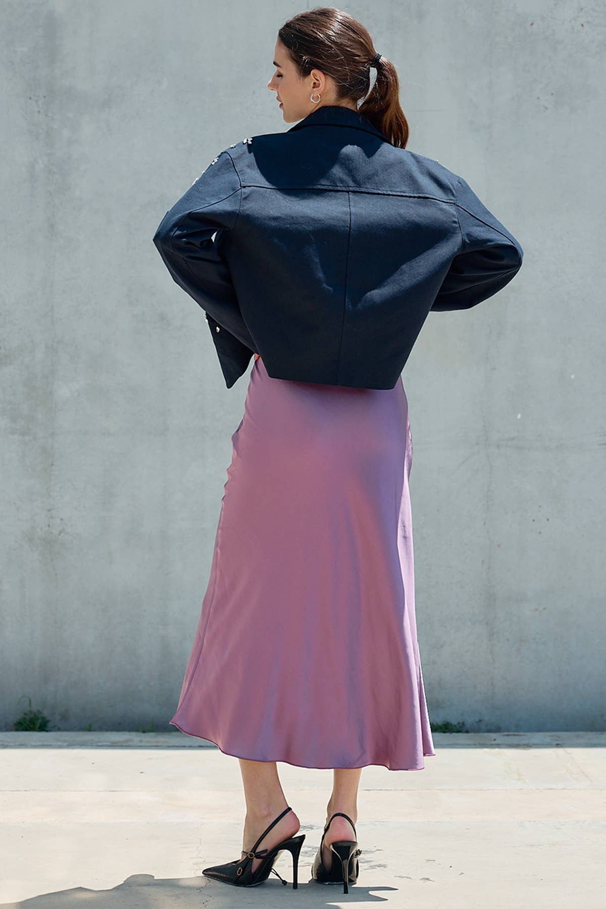 Woman wearing a navy cropped jacket and pink satin midi skirt with black heels