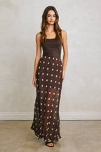 Woman wearing a black tank top with a sheer brown polka dot maxi skirt in women's clothing fashion.
