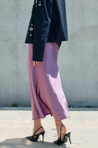 Woman wearing a flowing satin pink midi skirt with black heels and a dark embroidered jacket