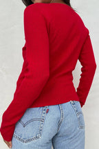 Woman wearing a fitted red long-sleeve knit top with subtle eyelet texture and light blue denim jeans from behind.