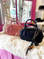 Three woven mini bags with handles and detachable straps in black, pink, and cream on a soft surface.