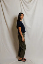 Woman wearing a navy cropped top and olive green pants standing against a neutral fabric backdrop