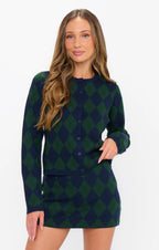 Woman wearing a soft knit navy and green argyle cardigan and matching skirt set in women’s clothing style