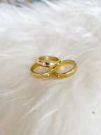 Three chunky gold rings with small embedded crystals resting on soft white fabric