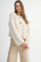 Woman wearing cream chunky knit sweater with gold buttons and beige wide-leg pants against white background
