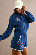 Woman wearing navy blue terry cloth hoodie and shorts with beach-themed embroidery and contrast trim accents in a relaxed fit
