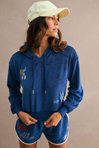 Woman wearing navy blue embroidered terry cloth hoodie and shorts with beach-inspired designs and a beige cap.