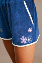 Close-up of blue terry fabric shorts with white trim and pink and white floral embroidery on the side, highlighting the texture of the Ciao Terry Hoodie fabric.