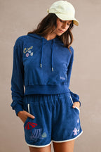 Woman wearing navy blue terry cloth lounge set with embroidered details and white trim, styled with a light yellow cap.