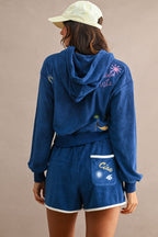Woman wearing blue terry cloth hoodie and Ciao Terry Shorts with white trim and embroidered back pocket, viewed from behind.