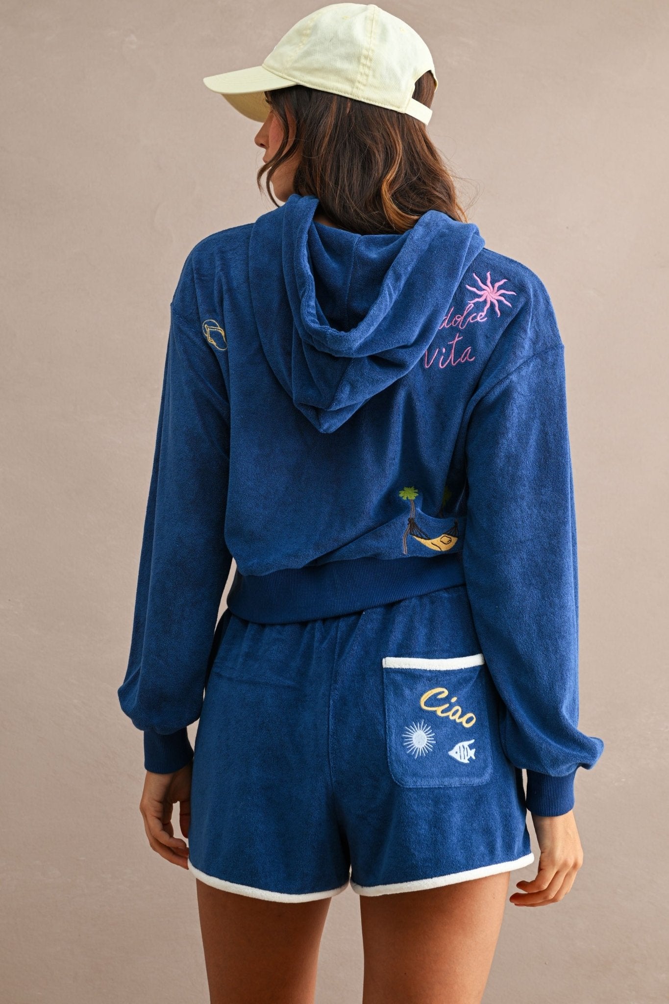 Woman wearing blue terry cloth hoodie and Ciao Terry Shorts with white trim and embroidered back pocket, viewed from behind.