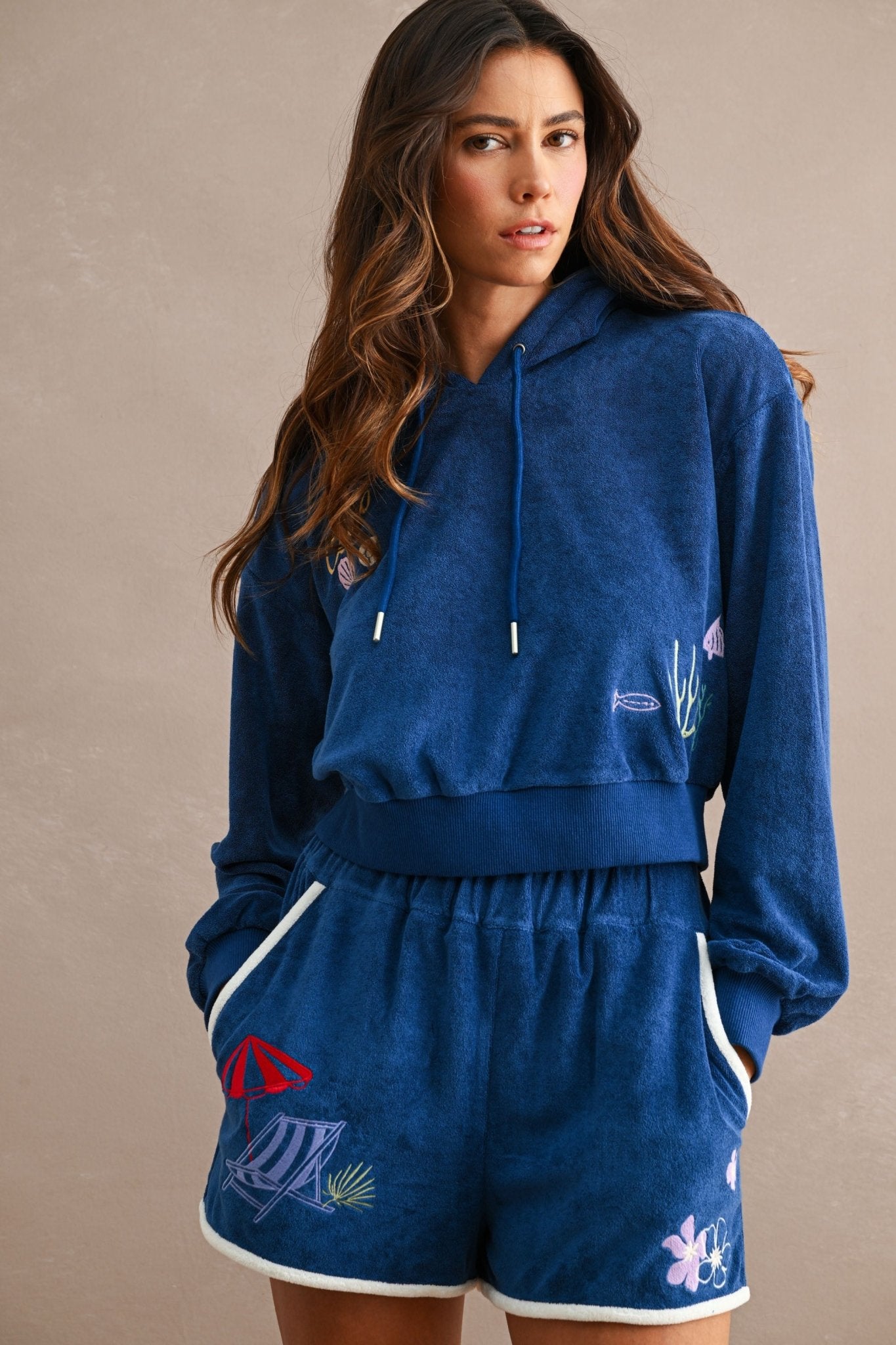 Woman wearing navy blue terry hoodie and matching Ciao Terry Shorts with beach-themed embroidered designs and white trim on pockets and hem.