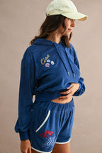 Woman wearing navy blue terry cloth shorts with embroidered beach umbrella and matching hoodie in women's clothing style