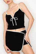 Woman wearing black two-piece outfit with white trim featuring a fitted top and wrap-style skort in women's clothing.