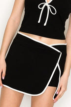 Woman wearing a black skort with white trim and a cropped black top with tie detail in women's clothing.