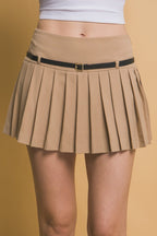 Close-up of a woman wearing a beige pleated mini skirt with a black belt against a neutral background