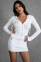 Woman wearing a white asymmetrical knit skirt and matching zip-up sweater in a stylish women's clothing outfit.