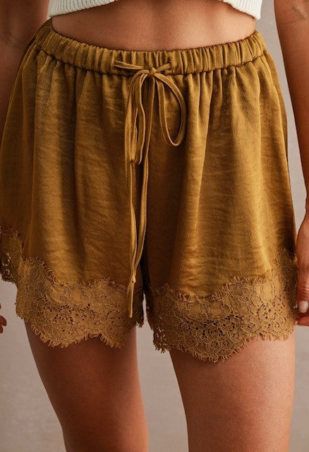 Close-up of women's mustard lace-trimmed shorts with elastic waistband and adjustable drawstring in soft fabric.